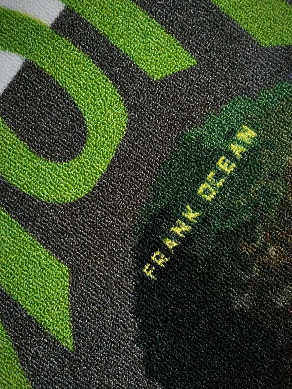 Blonde rug close-up showing the green hair detail with the artist name and partial album title, pixel-style weave