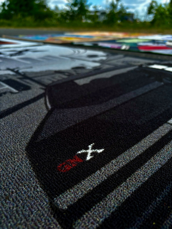 GNX rug – red logo focus GNX rug close-up from lower left, the red GNX logo in sharp focus with background rugs softly blurred